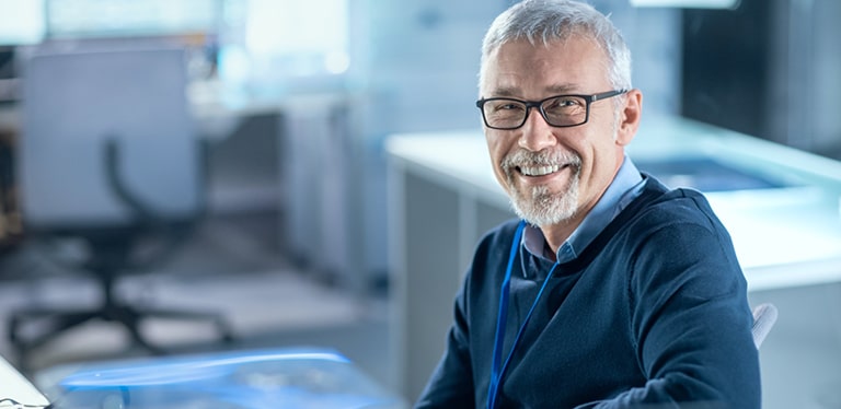 man in blue shirt and blue jumper with glasses smiling for the camera