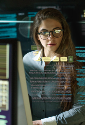 A professional woman stands at a digital workstation, interacting with layered data and interface screens in a modern, technology-driven environment, suggesting analysis or monitoring of complex information.