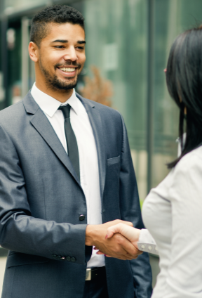 A person in a suit shakes hands with another individual outdoors in a modern business setting.