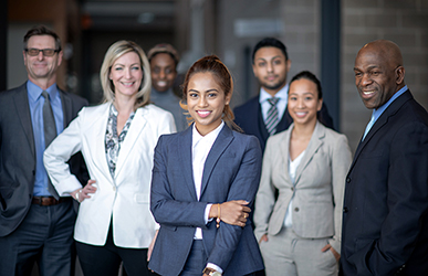 A diverse group of business professionals stand together in a modern office setting, wearing professional attire and projecting confidence and teamwork.