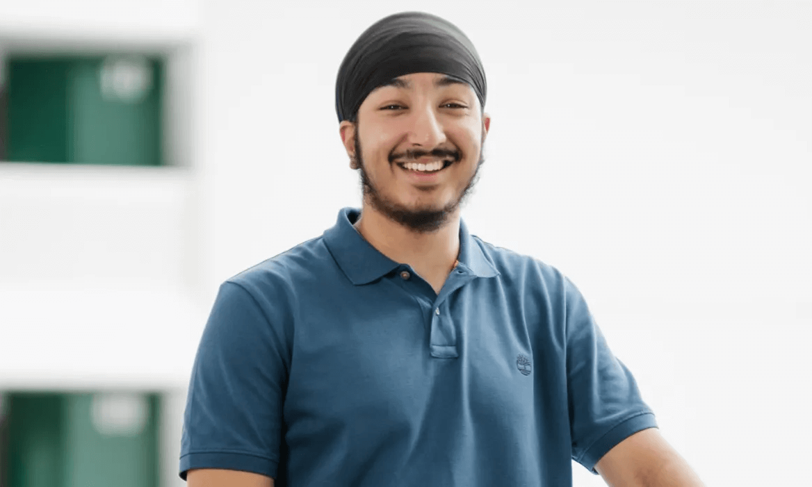 Smiling young man in a blue polo shirt standing against a white and green background