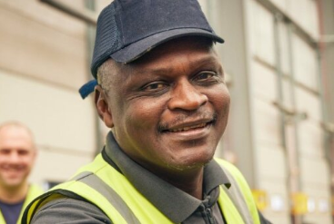 Smiling man in safety vest and cap near industrial area