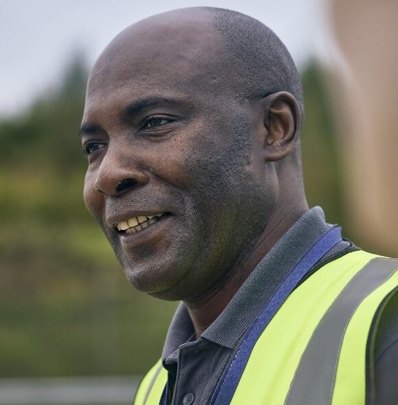 A person in a high-visibility safety vest and collared shirt stands outdoors