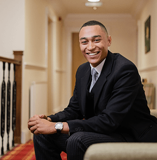 A formally dressed employee sits in a quiet, carpeted hallway with wooden railings