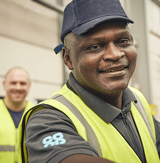 Two employees in high-visibility vests work in an industrial setting; one wears a cap and a Co-op branded shirt, with warehouse elements visible.