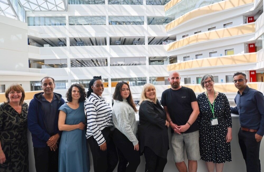 A diverse group of professionals standing together in a modern office atrium with multiple floors and glass ceilings