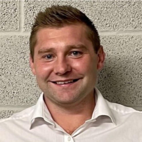 Man in white shirt smiling in front of brick wall.