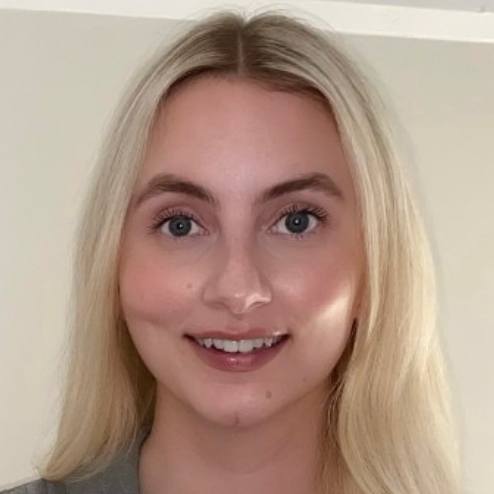 Smiling woman standing indoors against light wall.