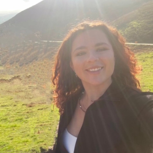 Smiling woman outdoors with sunlight in the background.