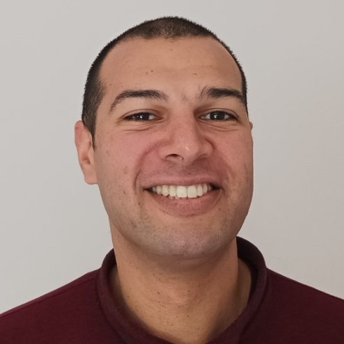 Man smiling in front of a plain light wall.