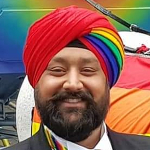 Man in rainbow turban smiling beside pride carriage.