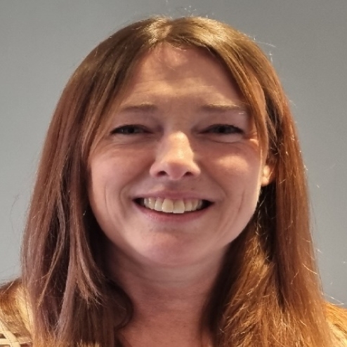 Smiling woman with long hair in front of gray wall.