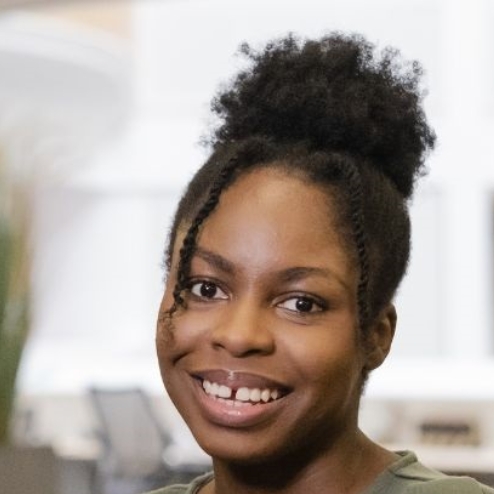 Smiling woman in an office setting with plants behind.