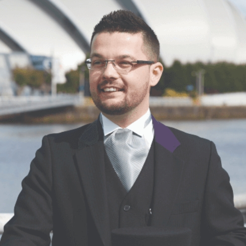 Man in formal wear standing by a riverside railing.