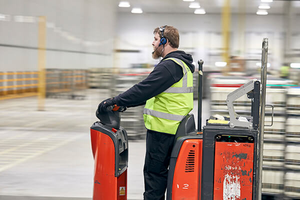 Person in a high-visibility vest using a red pallet jack in a warehouse.