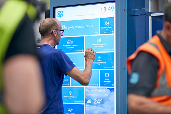 Person using a large Co-op digital screen showing news, safety info, and weather.