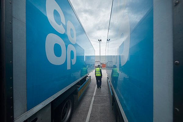 Person in a high-visibility vest walking between two Co-op lorries under an overcast sky