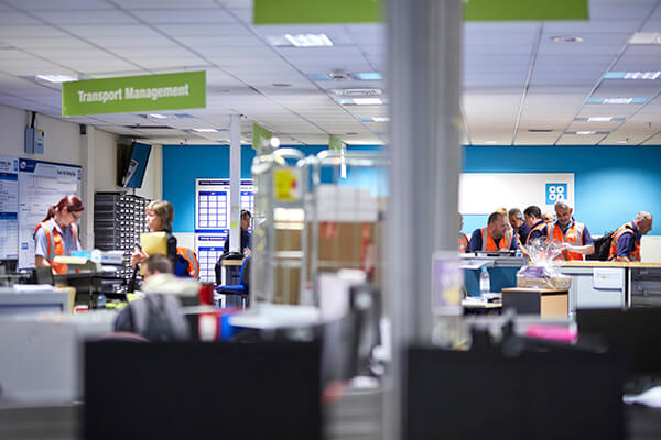 People in high-visibility vests in an office under a 'Transport Management' sign.