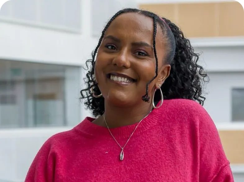 Individual wearing a headset in an office or call center setting, with other people and computer screens visible in the background