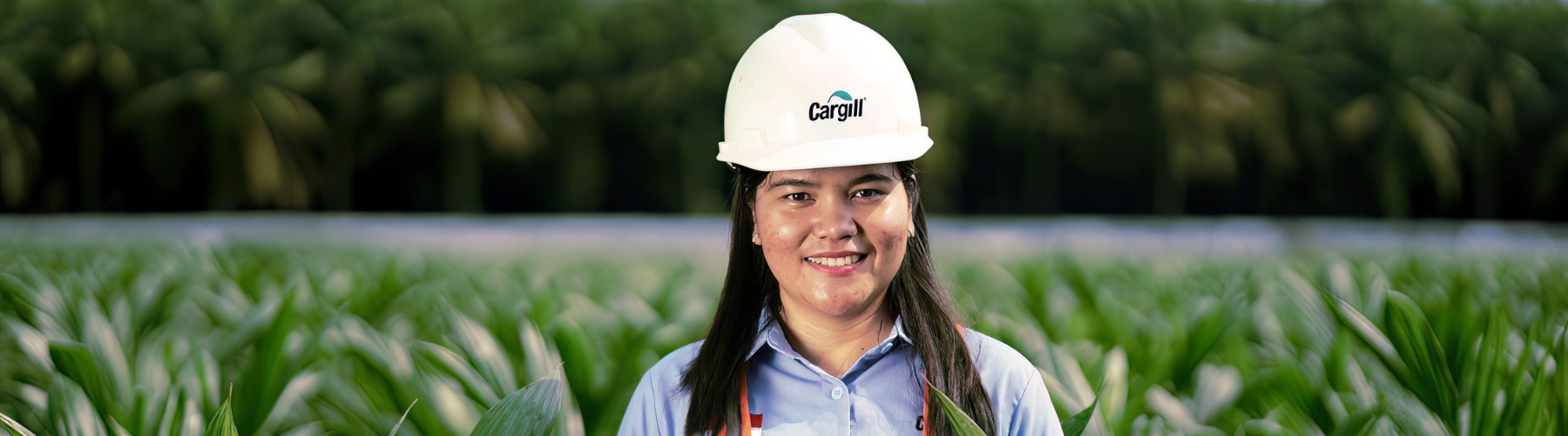 Cargill employee wearing a hard hat and safety vest standing in a green agricultural field.