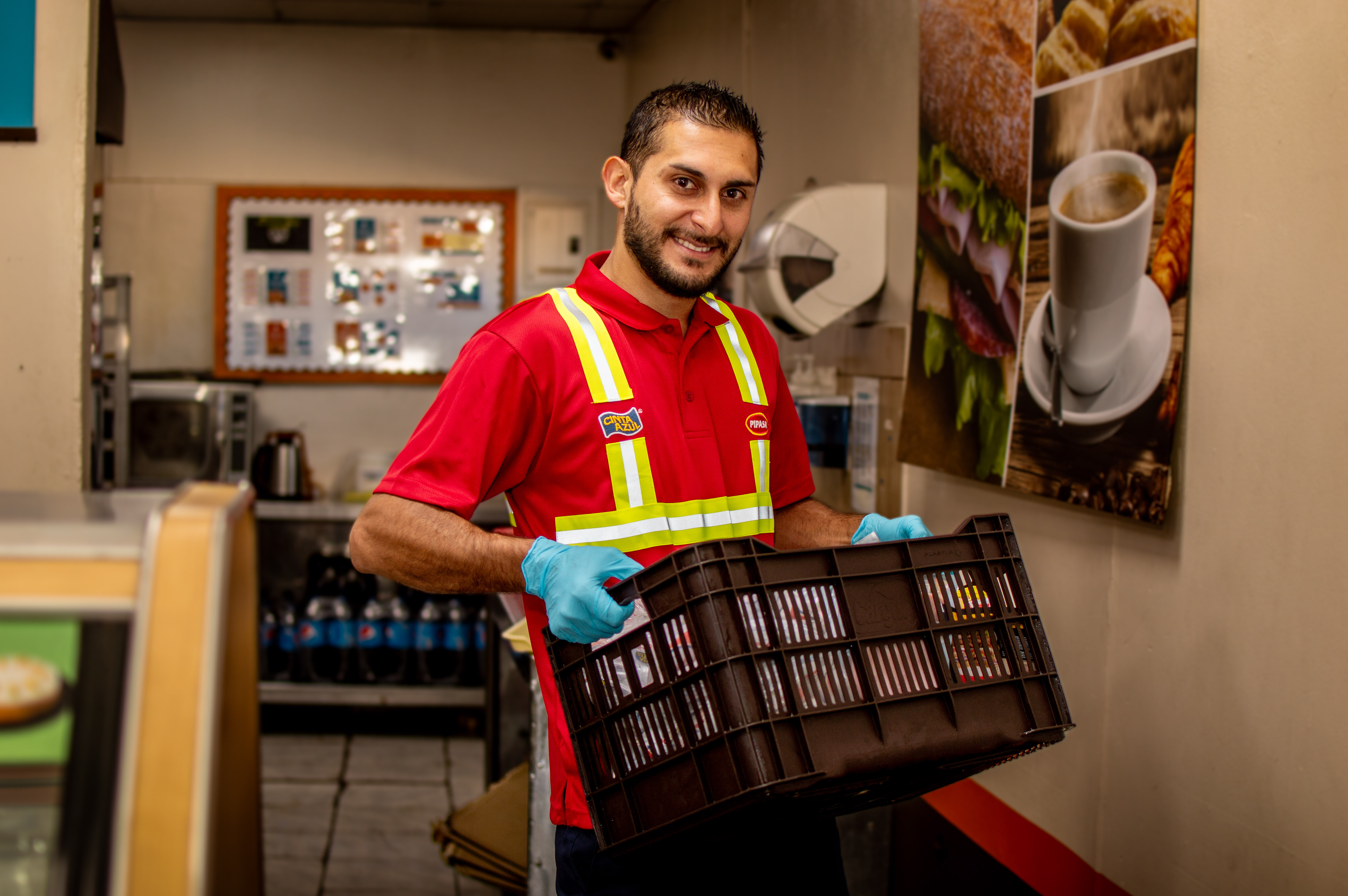 Colaborador de Cargill con uniforme de trabajo, chaleco de alta visibilidad y guantes, transportando una caja de productos alimenticios en una instalación de servicio y distribución.