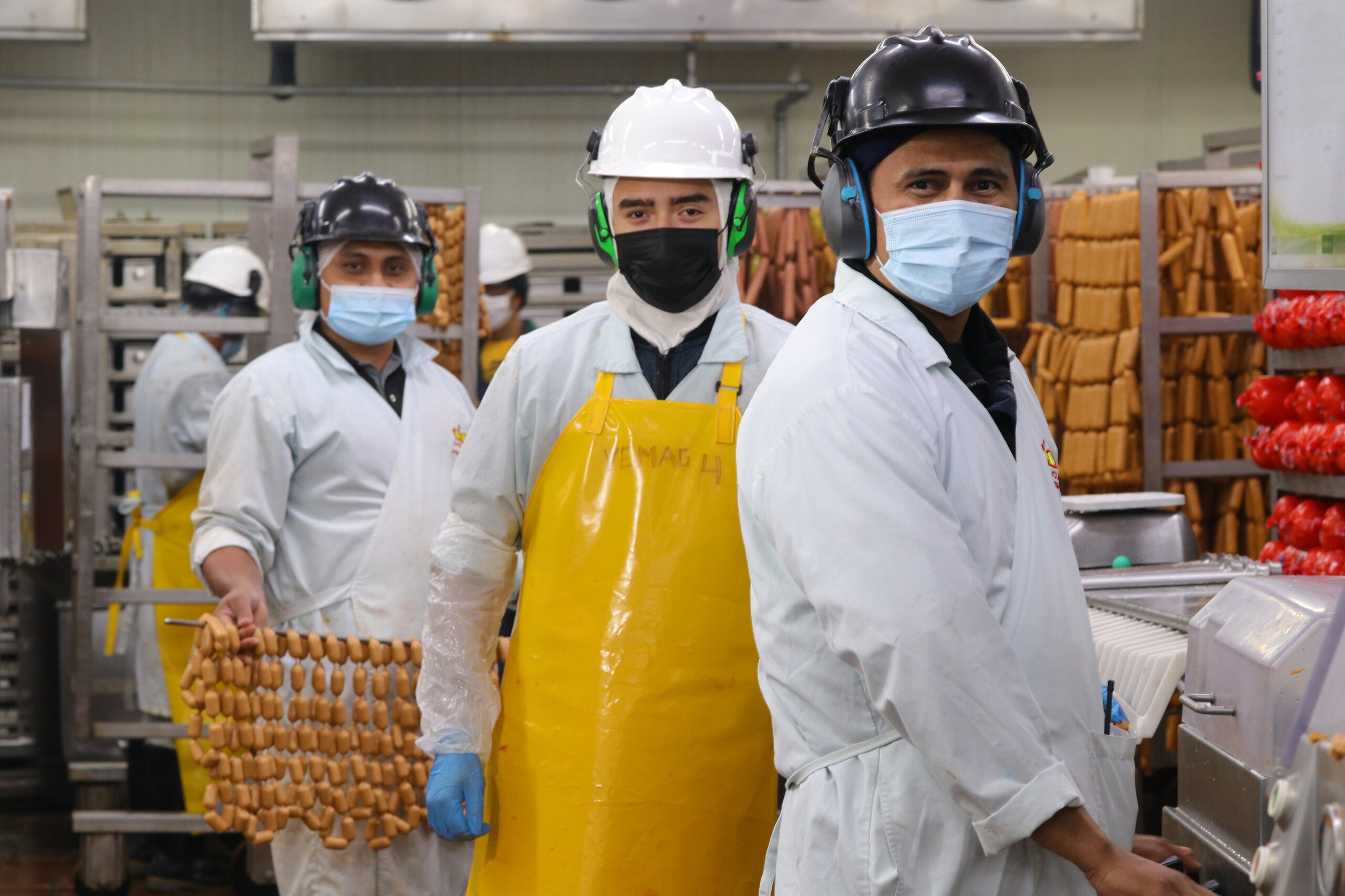 Colaboradores de Cargill con ropa de protección, cascos, protección auditiva y mascarillas en una planta de producción de alimentos.