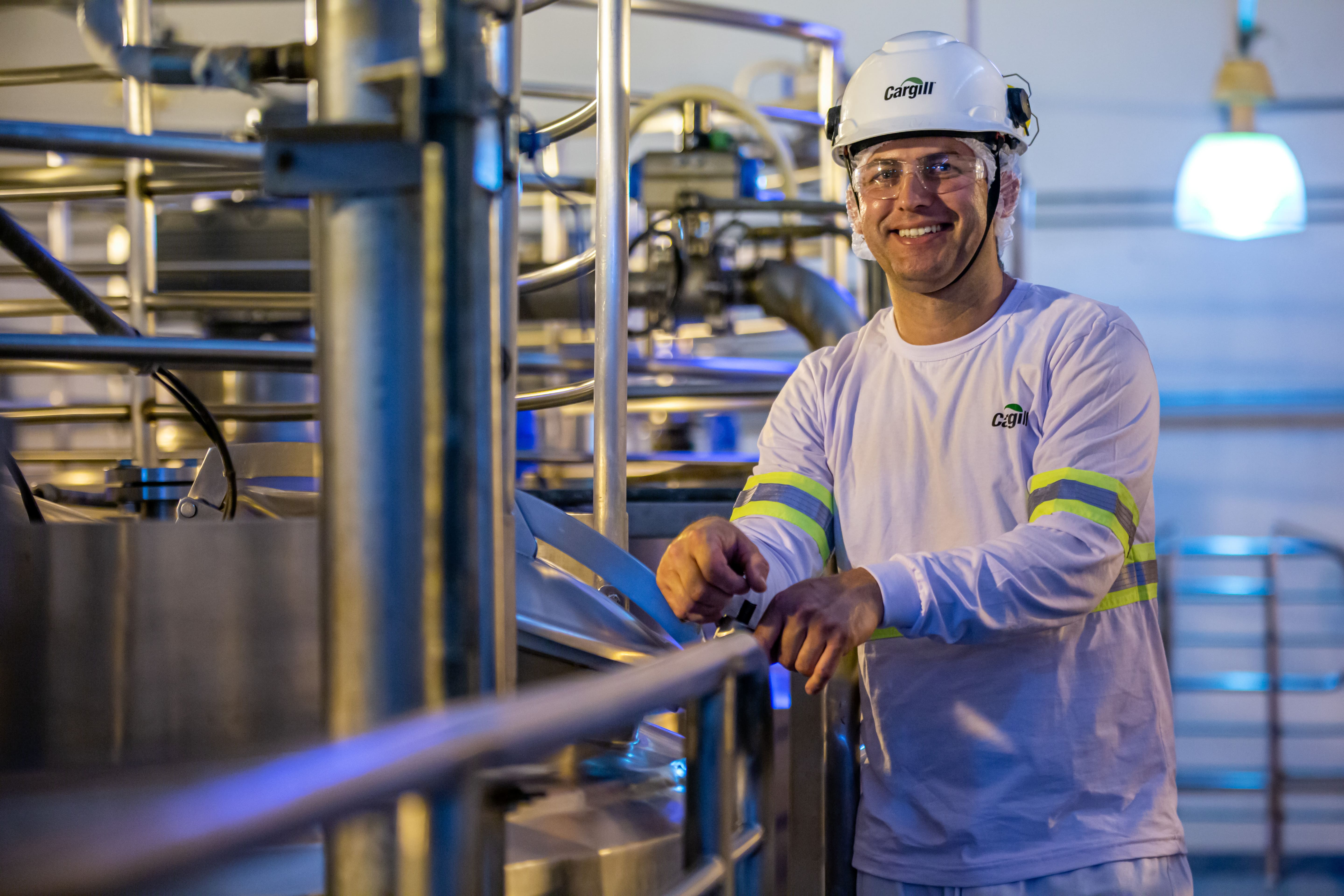 Colaborador de Cargill con casco y lentes de seguridad operando equipos de procesamiento industrial en una planta de manufactura.