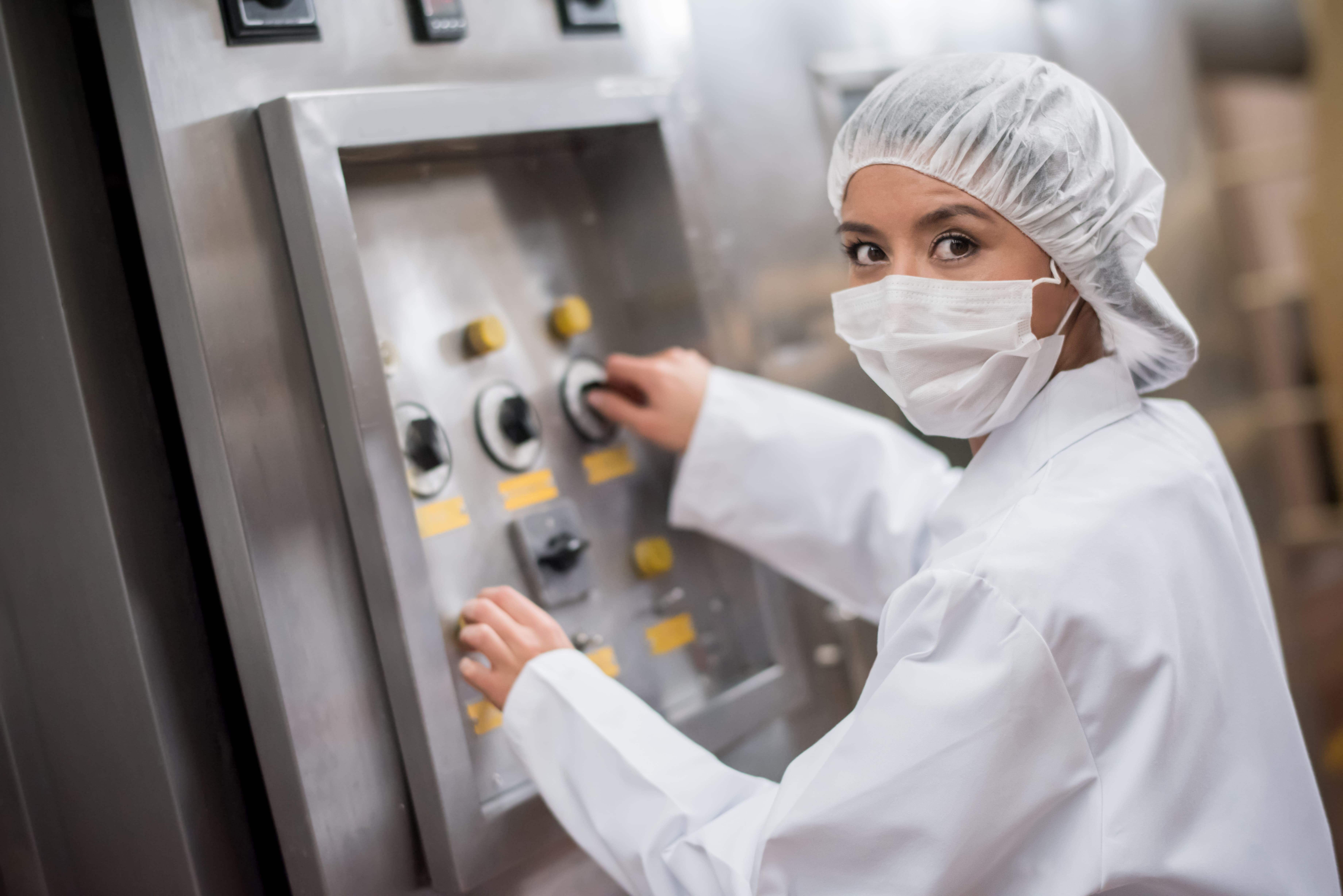 Colaborador de Cargill con equipo de protección sanitaria y cubrebocas operando un panel de control de producción en una planta de manufactura de alimentos.