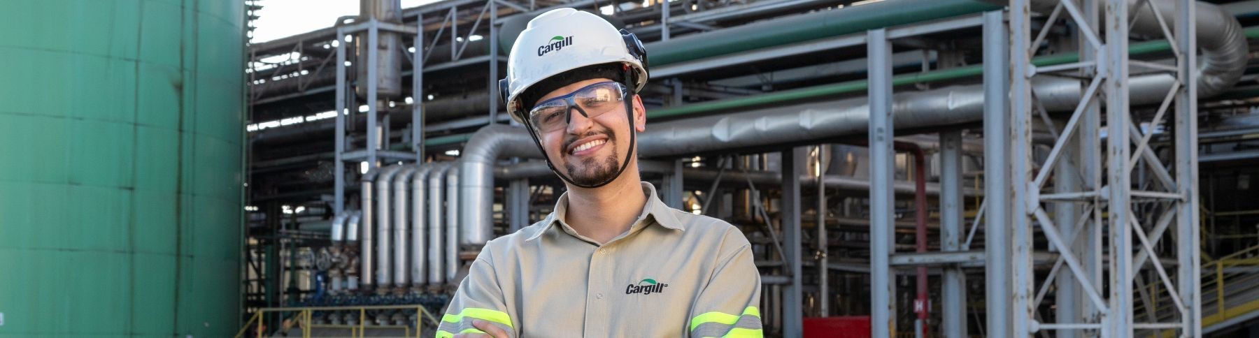 Cargill employee wearing a hard hat, safety glasses and high-visibility workwear standing in front of industrial processing equipment at a manufacturing facility.