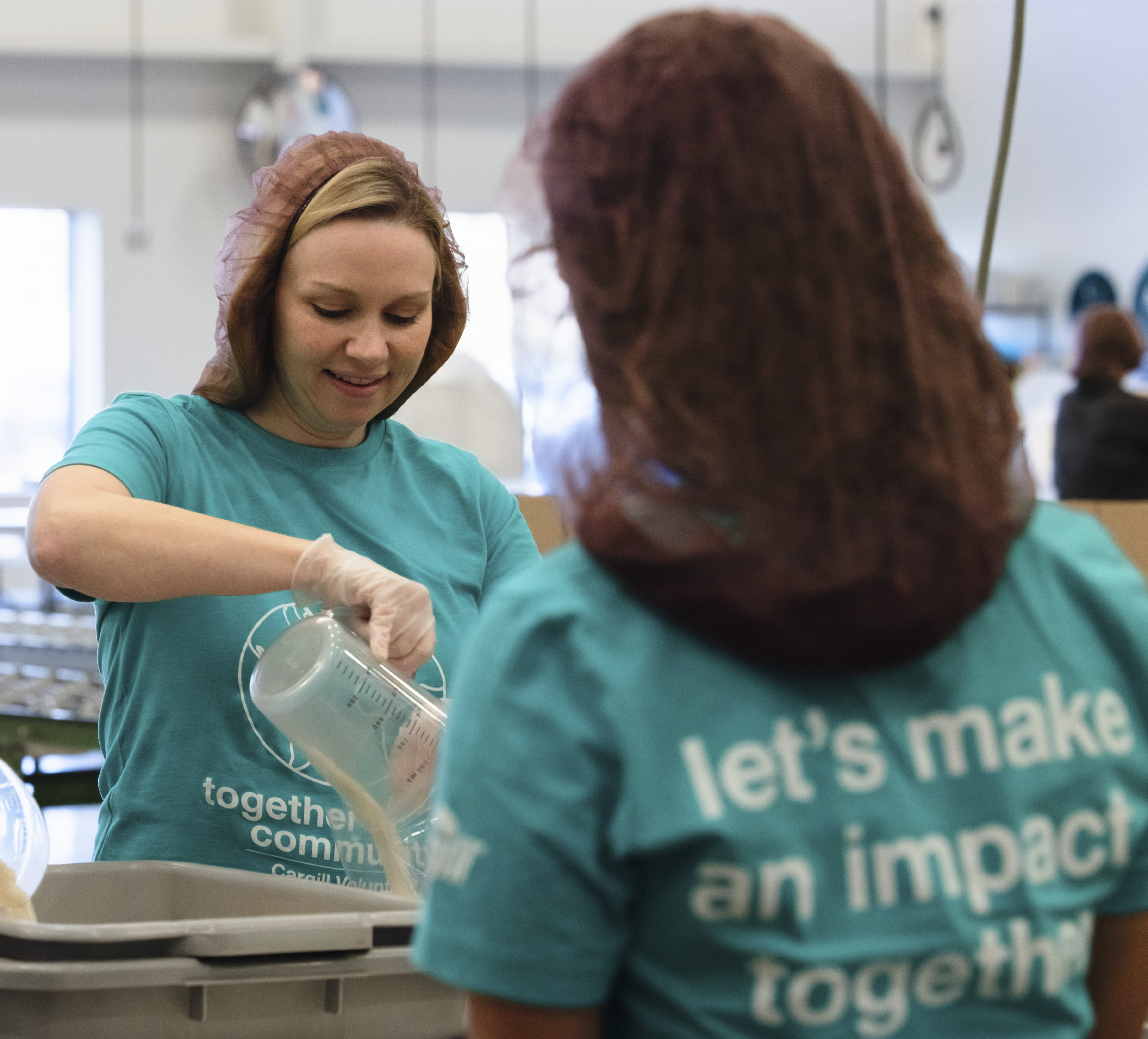 Two Cargill volunteers wearing matching community outreach T-shirts work together at a volunteer event, preparing materials at a packaging station.