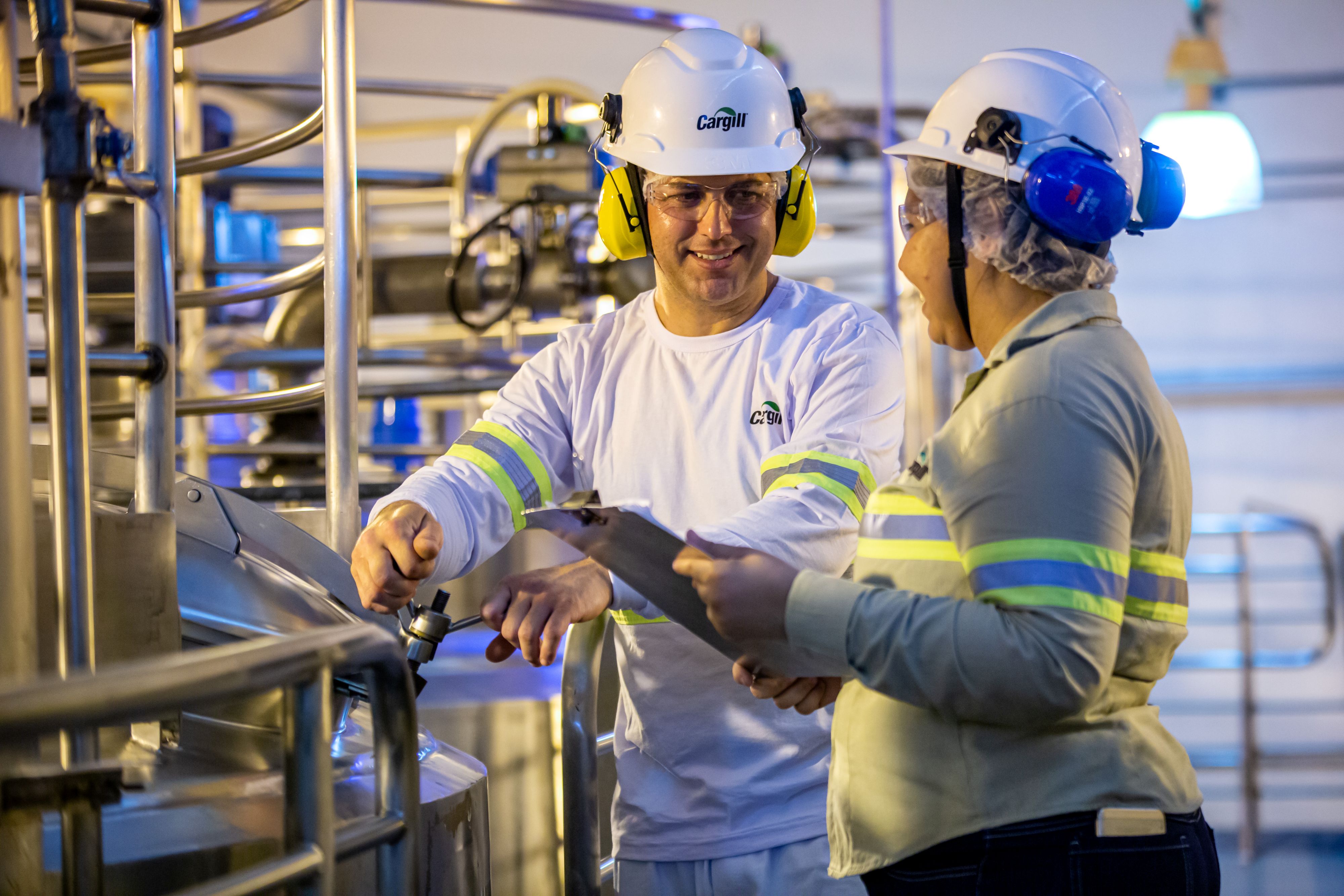 Cargill manufacturing employees working together near industrial processing equipment while wearing personal protective equipment and reviewing operations.