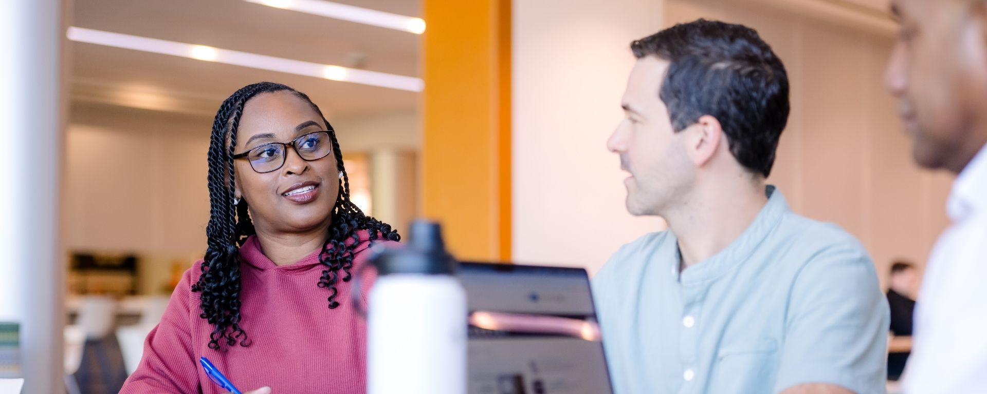 Two Capital One associates talking to one another with laptop and pencil and paper on table
