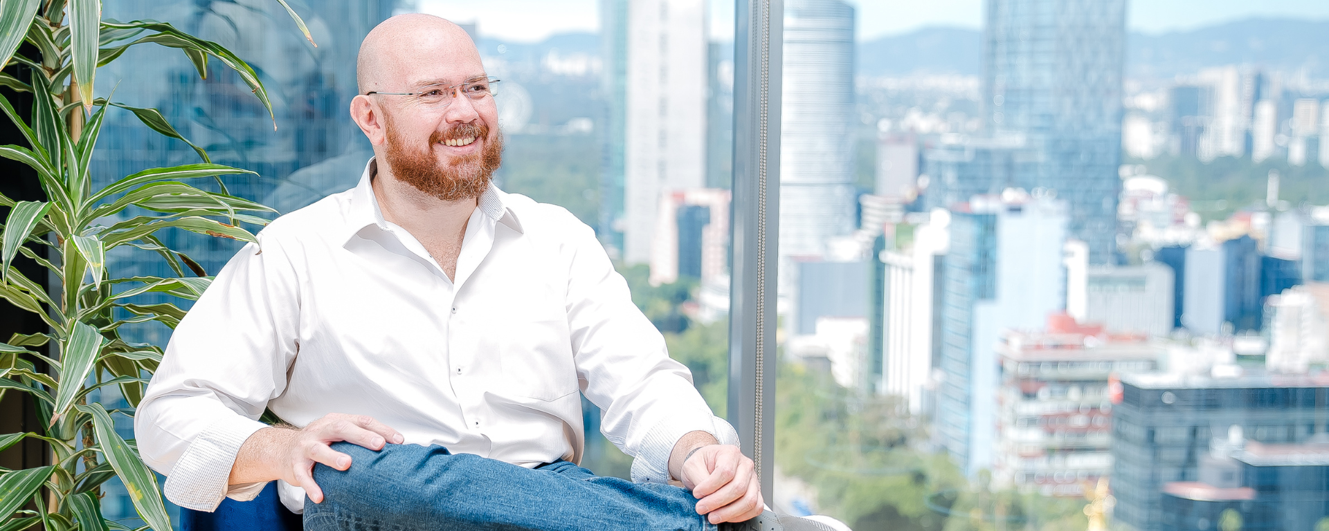Capital One associate Arturo sits in a blue sofa chair with ankle crossed over knee and smiles