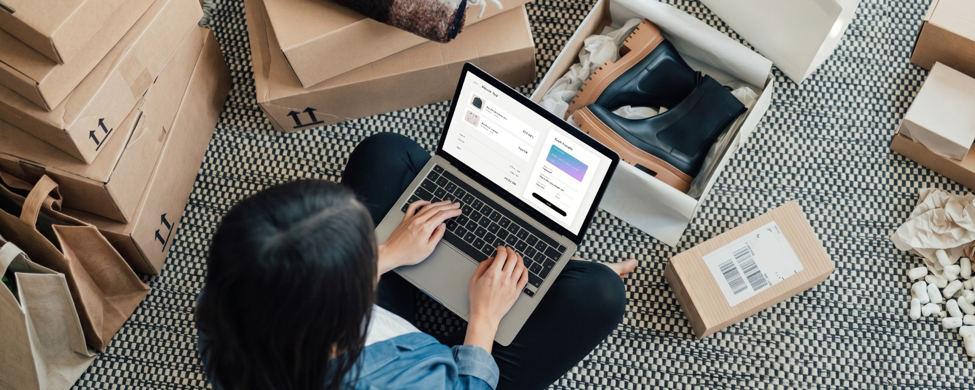 Bird's eye view of a customer sitting cross-legged on the floor surrounded by boxes and a laptop in their lap while shopping online
