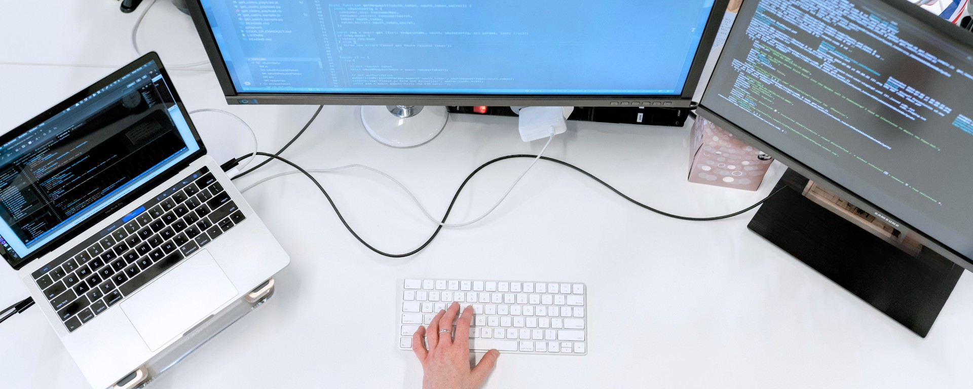 A hand typing on a keyboard connected to monitors and a laptop