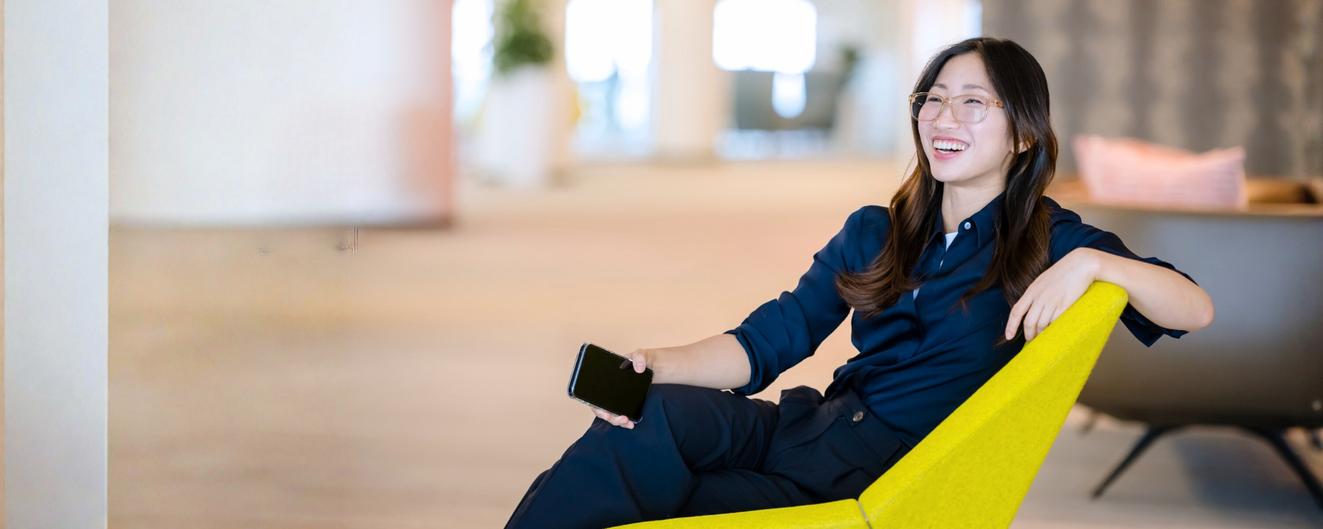 Capital One associate smiling in a yellow sofa chair with phone in hand
