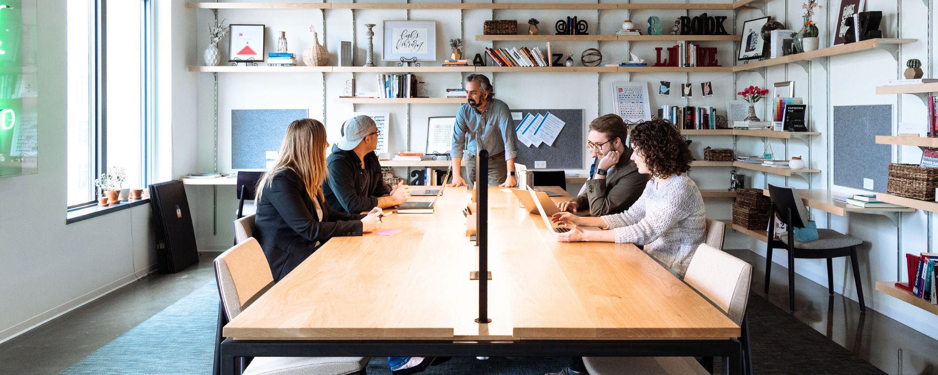 Four associates sit at a desk as a peer leans on the table and speaks to them