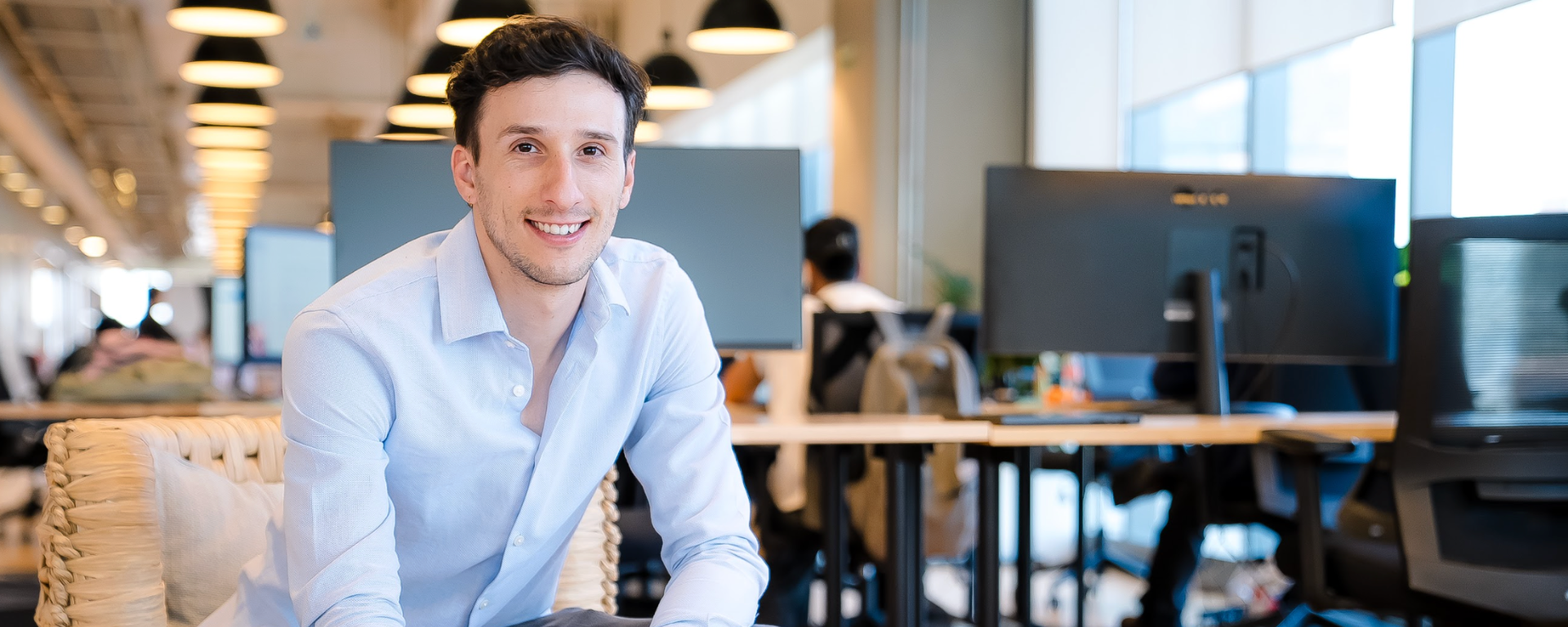 Capital One associate Javier sitting at a circular table and writing in a notebook while smiling at the camera