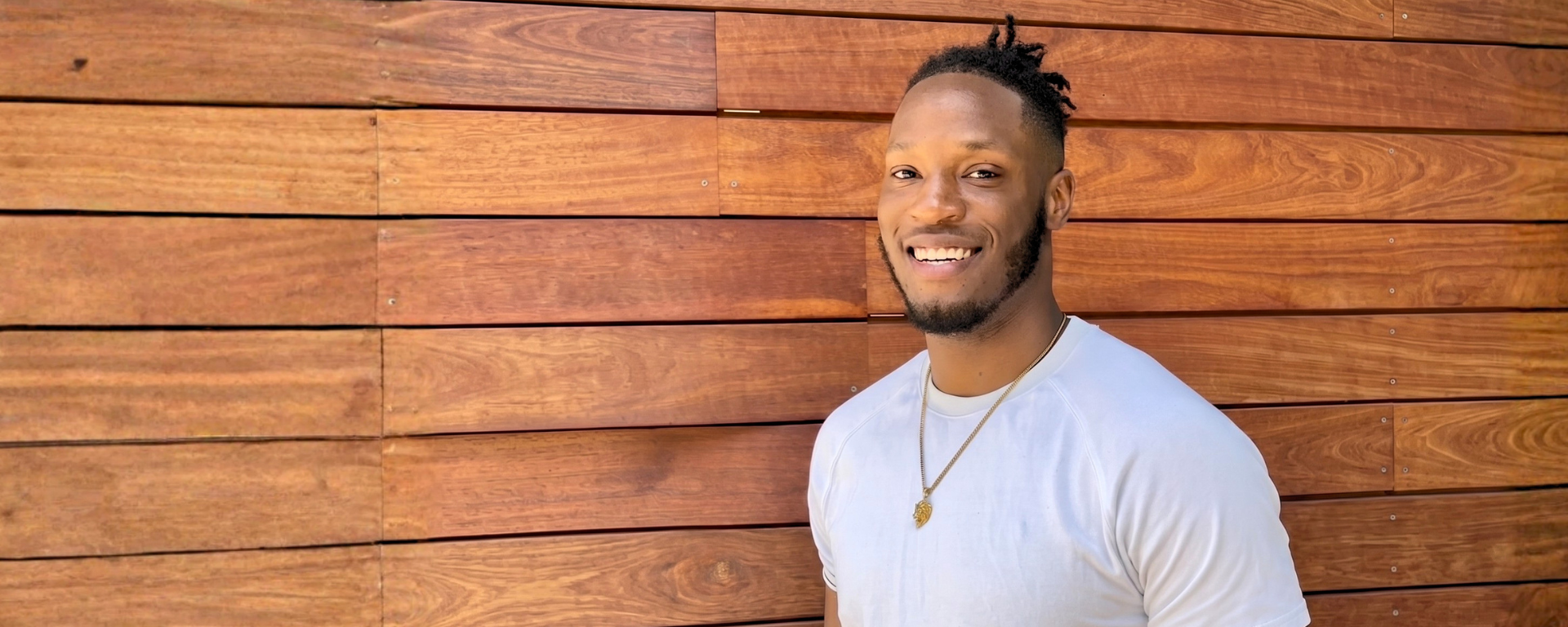 Capital One associate Kadeem smiles in a white tshirt against a wood backdrop