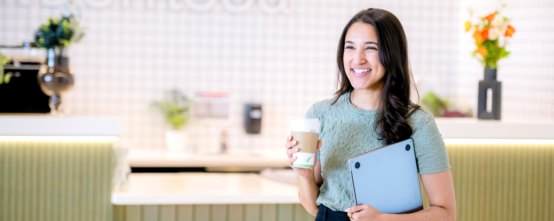 Capital One associate Marina smiling and holding a coffee and a laptop in her arms