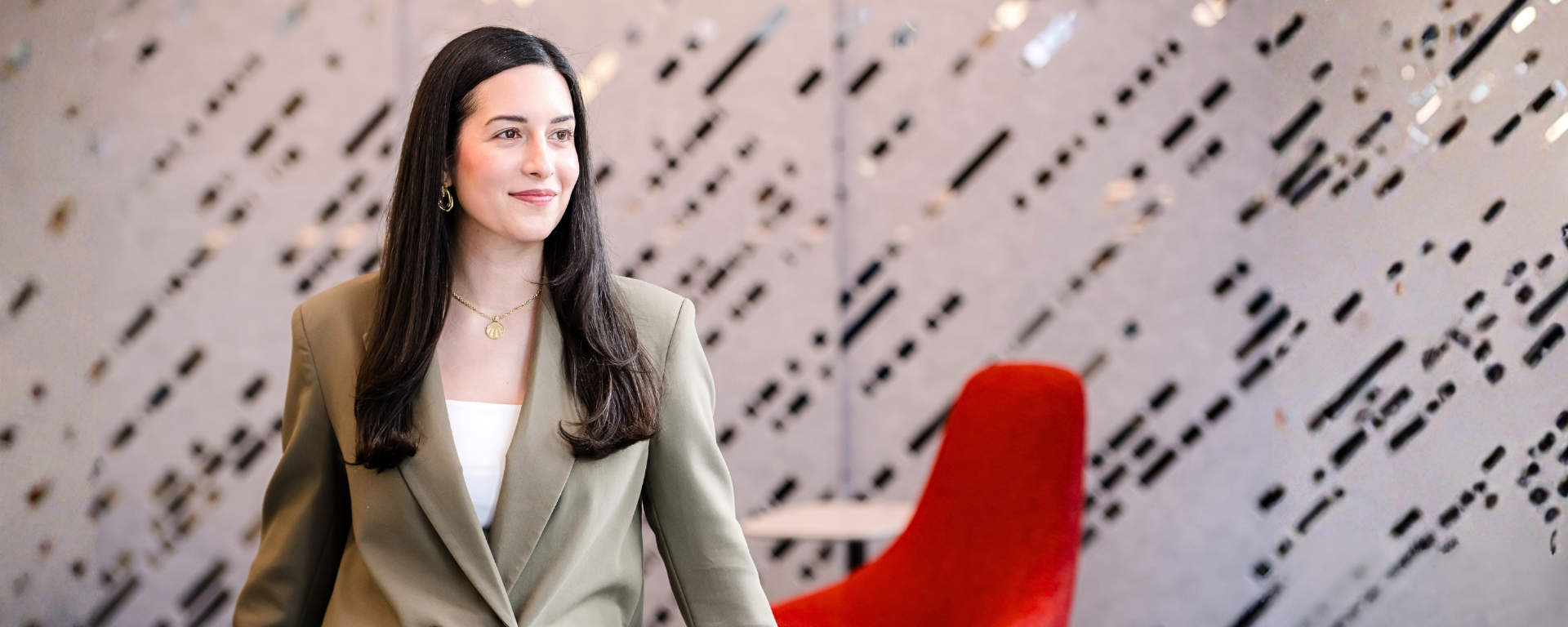 Capital One leader Monica wears a taupe colored blazer over a white shirt, looking to her left while walking through the office