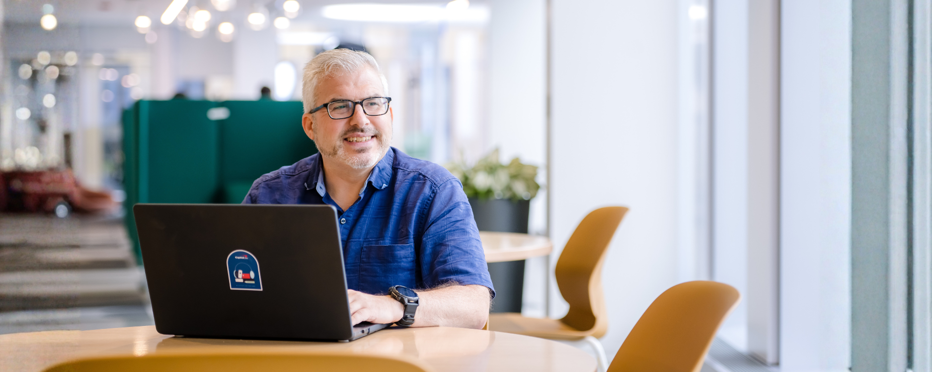 Capital One associate Ron sits at desk with laptop and gazes out the window