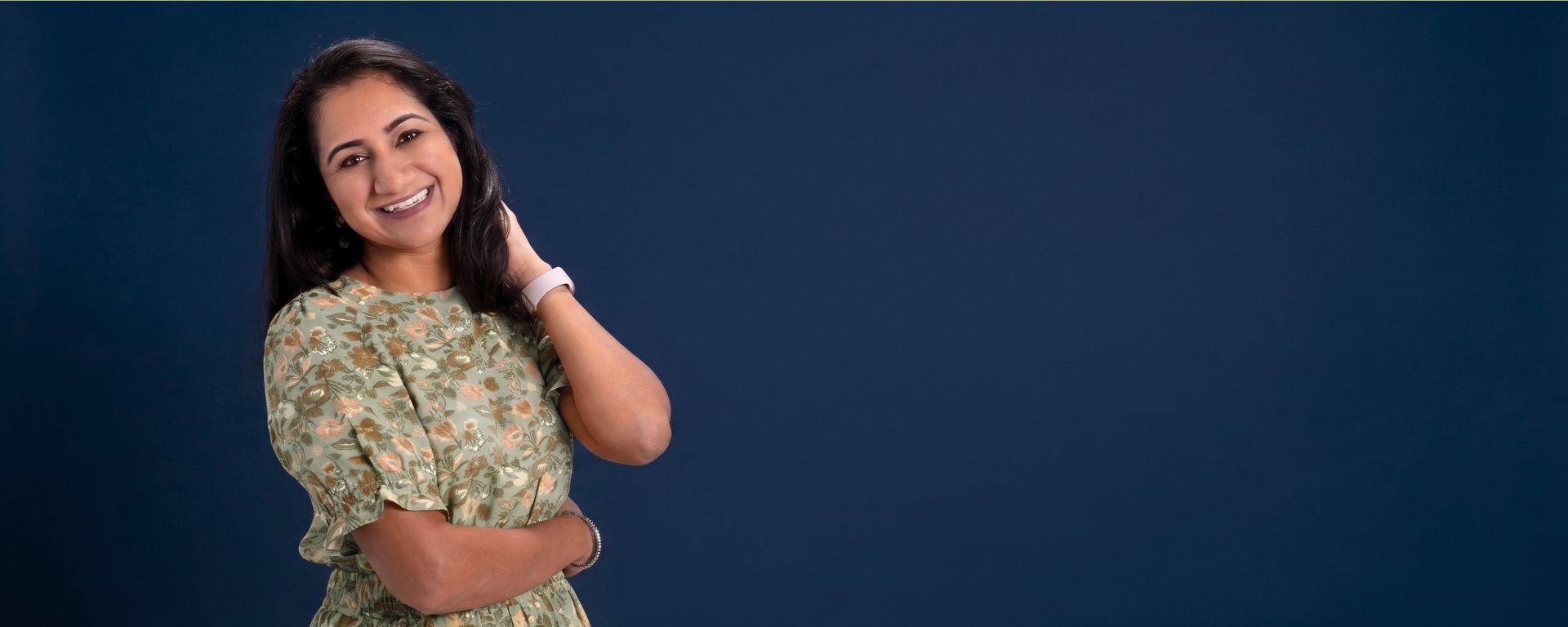 Capital One associate Shalini stands and smiles wearing a green floral dress in front of a blue background