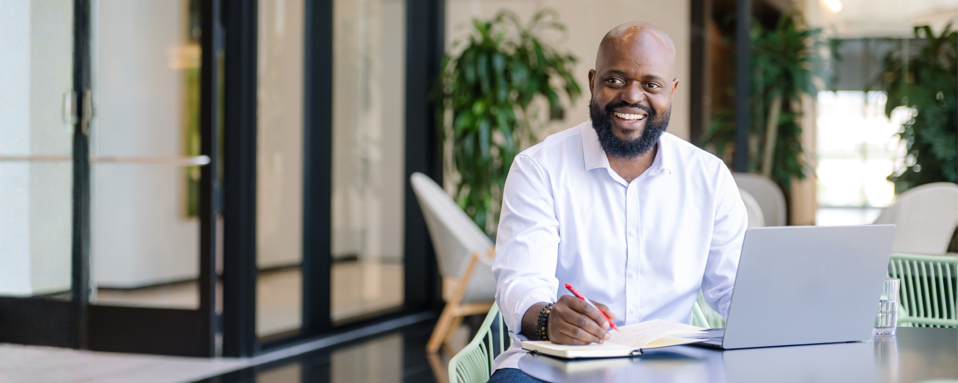 Capital One associate Tabot sits at a table with his laptop open and pen over notebook