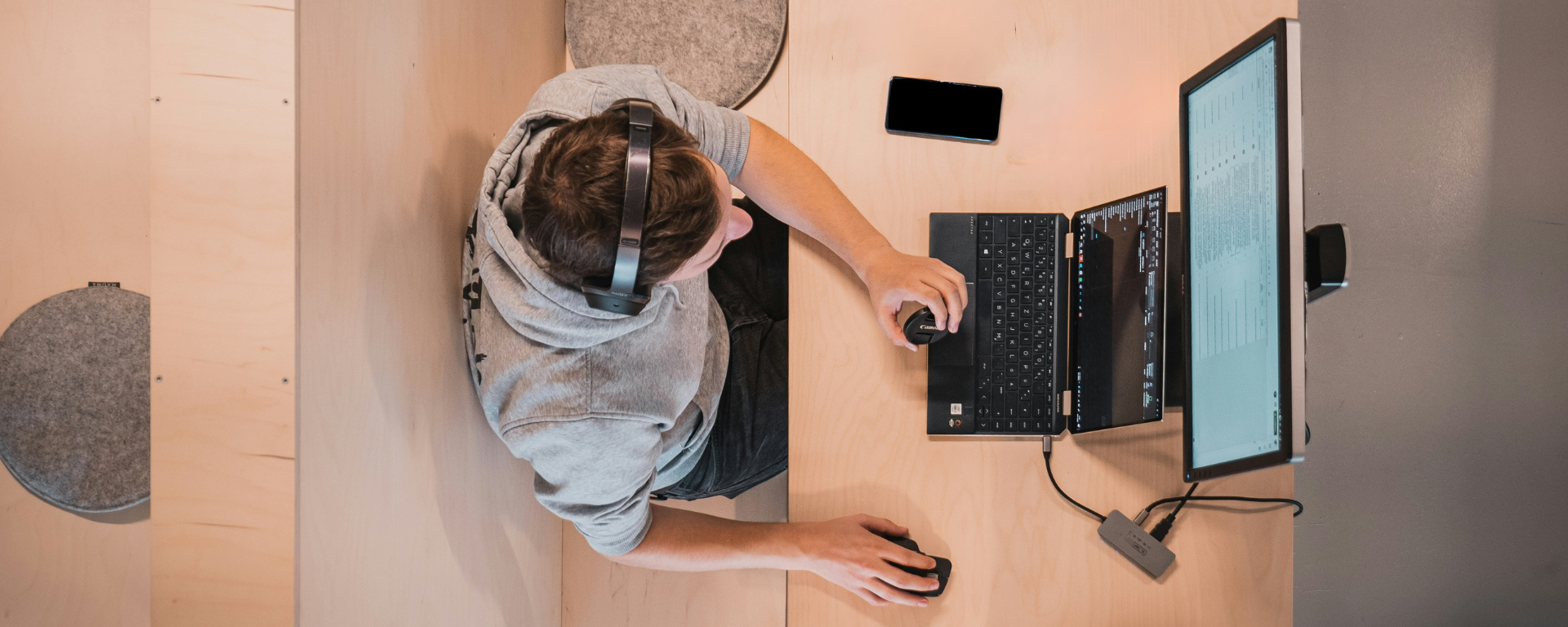 Bird's eye view of an associate wearing a hoodie and headphones while working on his laptop and monitor