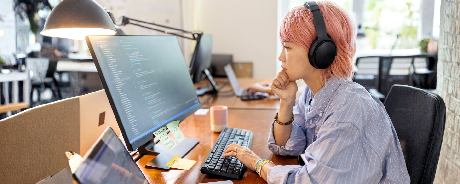 An associate coding on their desktop with headphones on