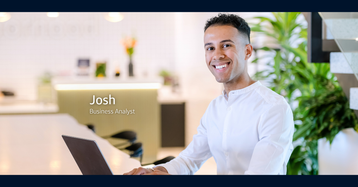 Josh, Business Analyst at Capital One, smiles at the camera while working on his laptop in a cafe