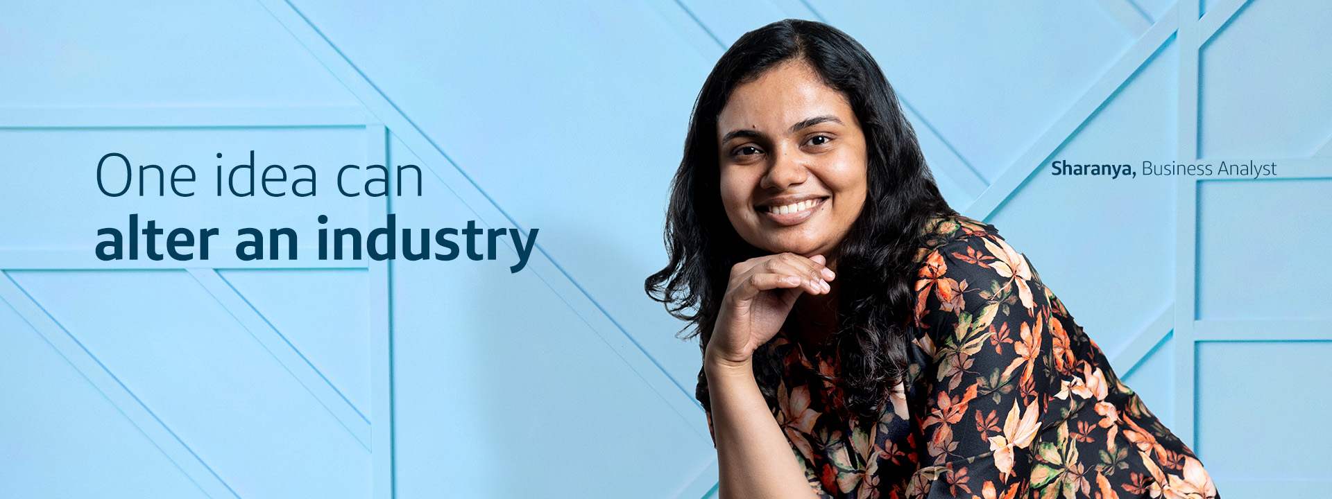 Capital One India associate Sharanya, Business Analyst, leans over and smiles in front of a light blue wall, next to the title "One idea can alter an industry"