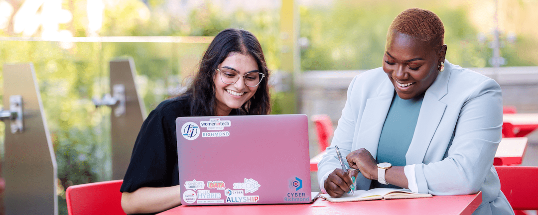Two Capital One associates sit outside at a red talbe and work together on a laptop