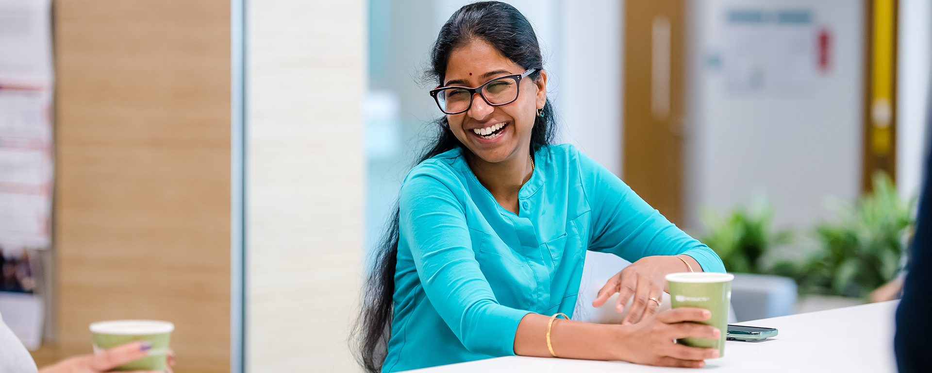 Capital One associate in a bright blue shirts sits holding a matcha and laughs